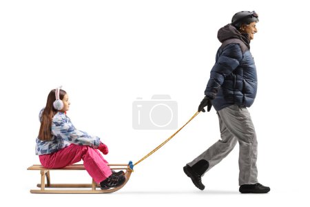 Foto de Full length profile shot of a man in winter clothes pulling a girl on a wooden sleigh isolated on white background - Imagen libre de derechos
