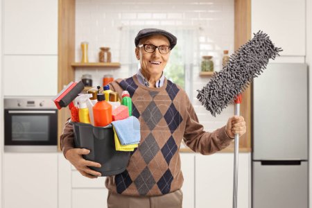 Photo for Elderly man holding a bucket with cleaning supplies and a floor mop inside a kitchen - Royalty Free Image