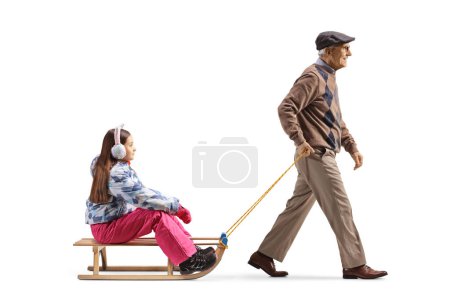 Foto de Full length profile shot of a senior man pulling a girl with a wooden sleigh isolated on white background - Imagen libre de derechos