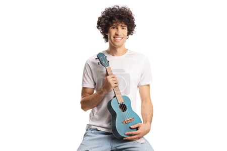 Foto de Young man with curly hair sitting and holding ukulele isolated on white background - Imagen libre de derechos