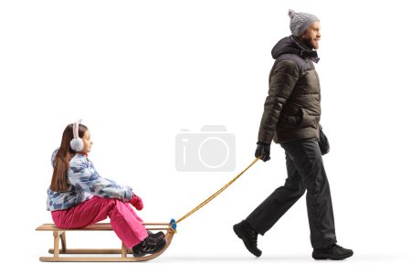 Foto de Full length profile shot of a father pulling a girl with a wooden sleigh isolated on white background - Imagen libre de derechos