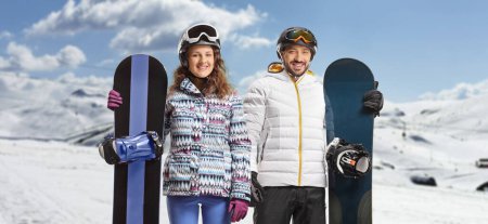 Foto de Young man and woman with snowboards posing on a snowy mountain - Imagen libre de derechos