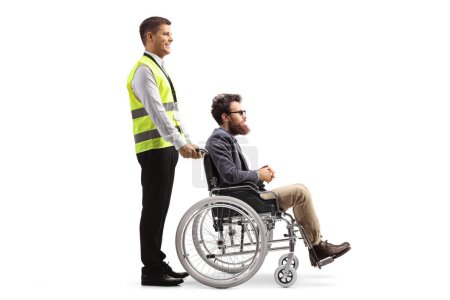 Foto de Foto de perfil completo de un trabajador del aeropuerto de asistencia especial con un pasajero masculino en una silla de ruedas aislado sobre fondo blanco - Imagen libre de derechos