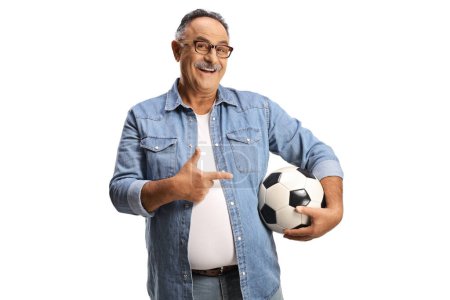Téléchargez les photos : Homme mûr souriant tenant un ballon de football et pointant isolé sur fond blanc - en image libre de droit
