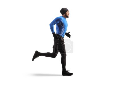 Foto de Foto de perfil de longitud completa de un hombre joven en forma corriendo en ropa de abrigo aislado sobre fondo blanco - Imagen libre de derechos