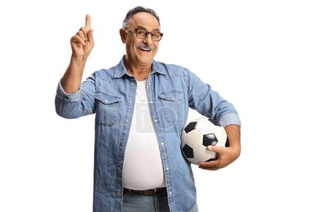 Téléchargez les photos : Homme mûr souriant tenant un ballon de football et pointant vers le haut isolé sur fond blanc - en image libre de droit