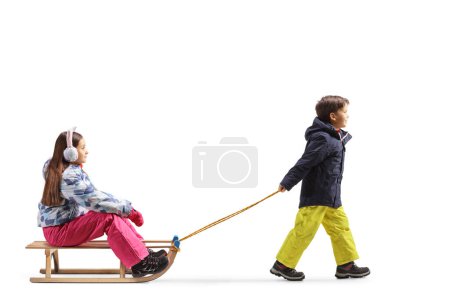 Téléchargez les photos : Plan de profil complet d'un garçon marchant et tirant une fille avec un traîneau en bois isolé sur fond blanc - en image libre de droit