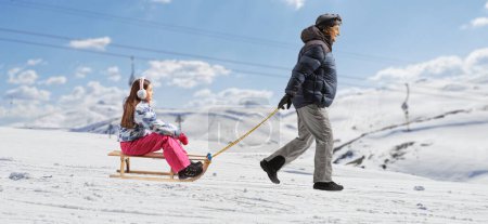 Téléchargez les photos : Man in winter clothes pulling a child with a sled on a mountain hill - en image libre de droit