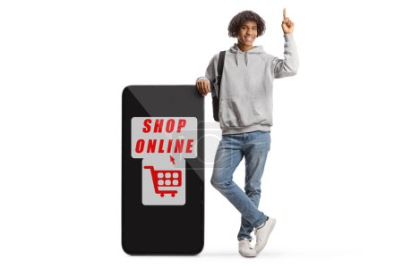Téléchargez les photos : Young african american male with a backpack leaning on a big mobile phone with text shop online isolated on white background - en image libre de droit