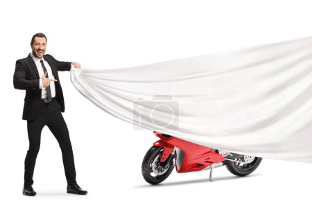 Foto de Hombre en traje y corbata sosteniendo un trozo blanco de tela delante de una moto roja y apuntando aislado sobre fondo blanco - Imagen libre de derechos