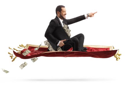 Photo for Businessman holding a briefcase with money sitting on a flying carpet and pointing isolated on white background - Royalty Free Image