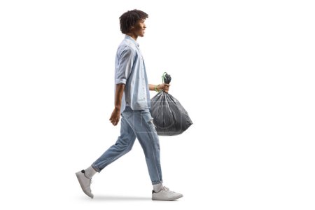 Photo for Full length profile shot of a casual african american man walking and carrying a plastic waste bag isolated on white background - Royalty Free Image