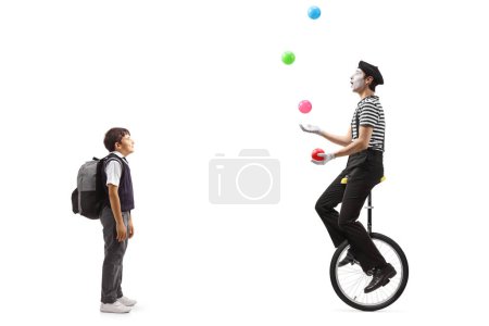 Téléchargez les photos : Plan complet d'un écolier regardant un mime jongler et chevaucher un monocycle isolé sur fond blanc - en image libre de droit