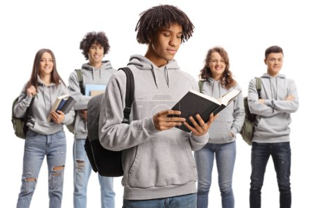 Foto de Estudiante afroamericano leyendo un libro y un grupo de estudiantes caucásicos de pie en la espalda aislados sobre fondo blanco - Imagen libre de derechos
