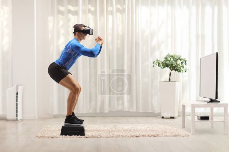 Foto de Full length profile shot of a man exercising with a stepper and wearing a vr headset in front of tv at home - Imagen libre de derechos