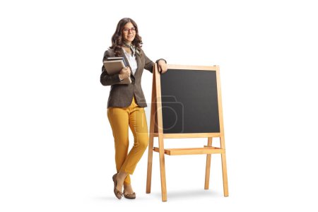 Ganztägiges Porträt einer jungen Lehrerin, die Bücher in der Hand hält und neben einer Tafel auf weißem Hintergrund steht