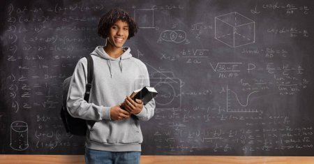 Photo for African american male student with a backpack holding books and standing in front of a blackboard - Royalty Free Image