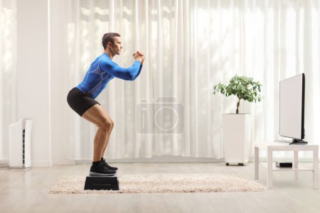 Foto de Tiro de perfil completo de un atleta masculino ejercitándose frente a la televisión en casa - Imagen libre de derechos