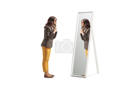 Téléchargez les photos : Full length profile shot of a young woman getting ready in front of a mirror and putting a scarf isolated on white background - en image libre de droit