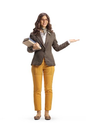 Full length portrait of a young female holding books and pointing with hand isolated on white background