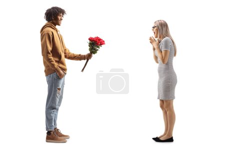 Téléchargez les photos : Full length profile shot of a young african american man giving a bunch of roses to a surprised caucasian woman isolated on white background - en image libre de droit