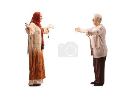 Foto de Foto de perfil completo de una mujer con un hiyab encontrándose con una anciana aislada sobre fondo blanco - Imagen libre de derechos