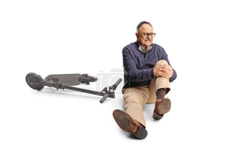 Photo for Mature man with an electric scooter holding his painful knee and sitting on the ground isolated on white background - Royalty Free Image