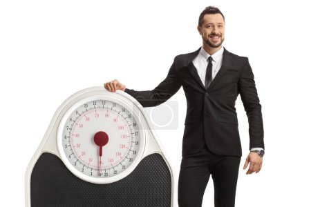Photo for Businessman in a suit and tie leaning on a big weight scale isolated on white background - Royalty Free Image