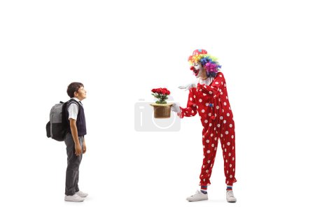 Téléchargez les photos : Écolier regarder un clown effectuer un tour avec chapeau et fleurs isolé sur fond blanc - en image libre de droit