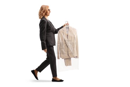Photo for Full length profile shot of a woman carrying suit on a hanger with a plastic dry cleaning bag isolated on a white background - Royalty Free Image