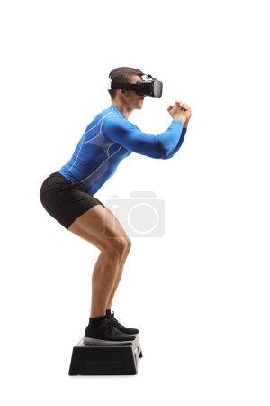 Téléchargez les photos : Plan de profil complet d'un homme portant un casque vr et s'exerçant avec une plate-forme aérobie pas à pas isolée sur fond blanc - en image libre de droit