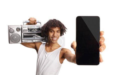 Téléchargez les photos : Jeune homme afro-américain tenant une boombox sur l'épaule et montrant un smartphone isolé sur fond blanc - en image libre de droit