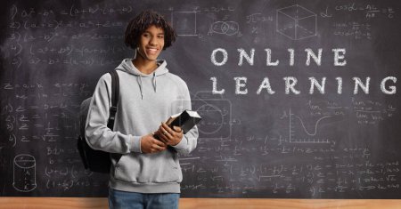 Photo for African american male student holding books in front of a blackboard text online learning - Royalty Free Image