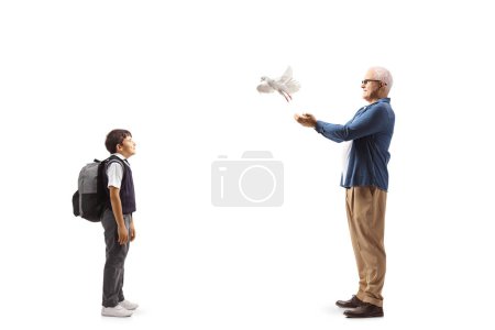 Téléchargez les photos : Photo de profil pleine longueur d'un écolier regardant un homme laisser une colombe blanche voler isolé sur fond blanc - en image libre de droit