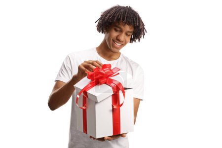 Téléchargez les photos : Heureux jeune homme afro-américain ouvrant une boîte-cadeau avec ruban rouge isolé sur fond blanc - en image libre de droit