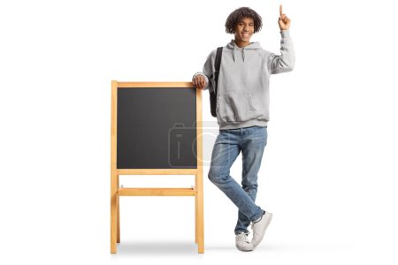 Photo for Full length portrait of an african american male student leaning on a blackboard and pointing up isolated on white background - Royalty Free Image