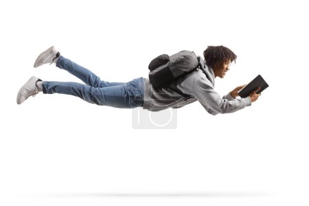Photo for Full length shot of an african american male student flying and reading a book isolated on white background - Royalty Free Image