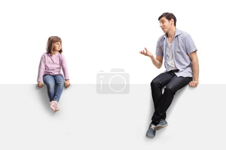Téléchargez les photos : Young man talking to a little girl and sitting on a blank white panel isolated on white background - en image libre de droit