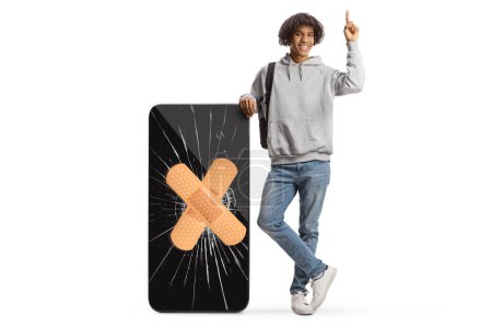 Téléchargez les photos : Young african american man leaning on a big mobile phone with cracked screen and bandage and pointing up isolated on white background - en image libre de droit