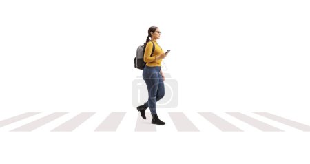 Téléchargez les photos : Étudiante sur un passage piétonnier marchant et écoutant de la musique depuis un smartphone isolé sur fond blanc - en image libre de droit