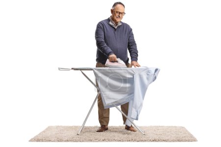 Téléchargez les photos : Mature homme repassage une chemise isolée sur fond blanc - en image libre de droit