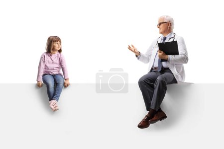 Téléchargez les photos : Male doctor talking to a little girl and sitting on a blank white panel isolated on white background - en image libre de droit