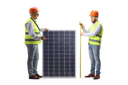Foto de Ingenieros masculinos midiendo un panel solar aislado sobre fondo blanco - Imagen libre de derechos