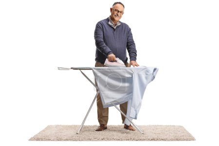 Téléchargez les photos : Mature man ironing a shirt and smiling isolated on white background - en image libre de droit