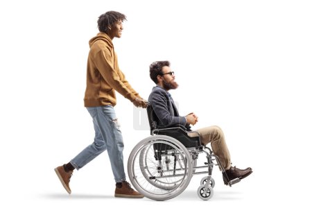 Téléchargez les photos : Full length profile shot of an african american young man pushing a caucasian man in a wheelchair isolated on white background - en image libre de droit