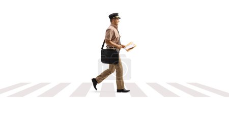 Photo for Full length profile shot of a mailman walking on a pedestrian crossing isolated on white background - Royalty Free Image