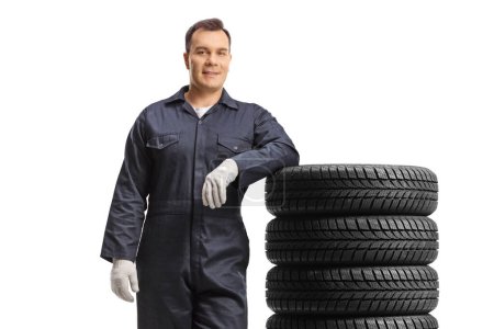 Téléchargez les photos : Mécanicien automobile en position uniforme et appuyé sur un tas de pneus isolés sur fond blanc - en image libre de droit