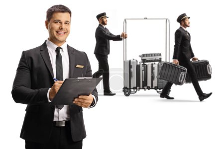 Téléchargez les photos : Receptionist holding a clipboard and bellboys carrying suitcases and pushing a luggage cart isolated on white backgroun - en image libre de droit