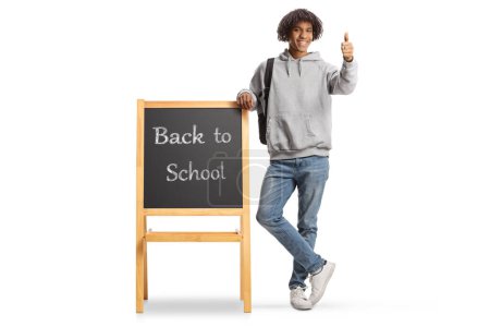 Photo for African american male student leaning on a blackboard with text back to school and gesturing thumbs up isolated on white background - Royalty Free Image
