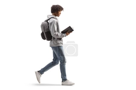 Photo for Full length profile shot of a young african american man walking and reading a book isolated on white background - Royalty Free Image